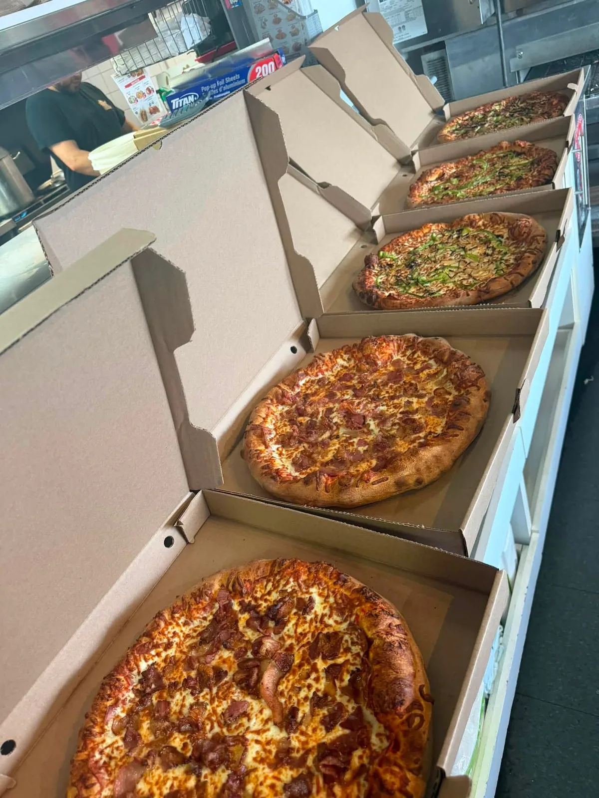 Boîtes de pizza ouvertes, alignées sur le comptoir du casse-croûte, prêtes à sortir.